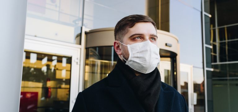 Man with medial mask standing outside offices