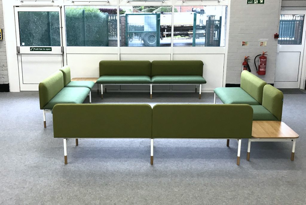 School office staffroom breakout space, with L-shaped corner sofas upholstered in green fabric