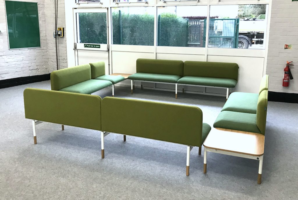 School office staffroom breakout space, with L-shaped corner sofas upholstered in green fabric