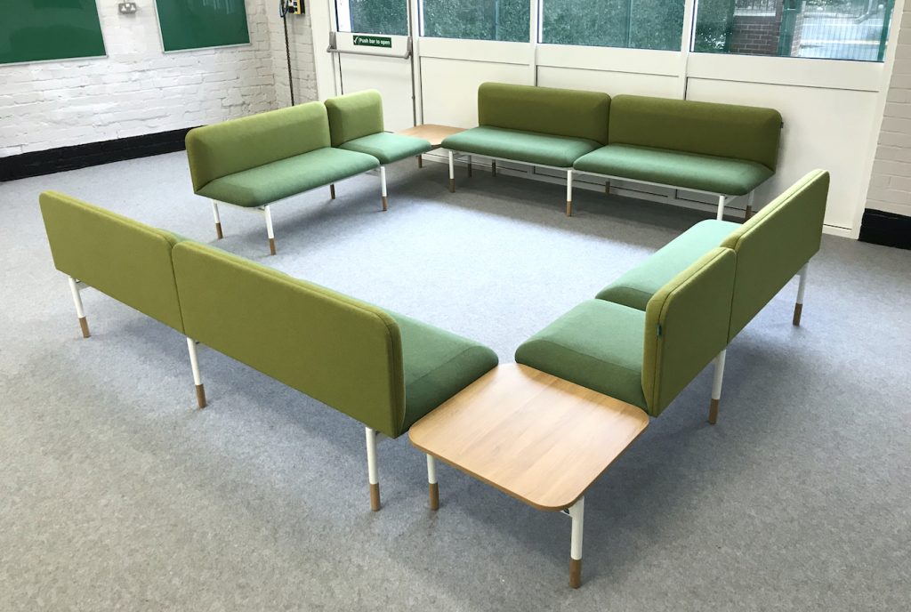 School office staffroom breakout space, with L-shaped corner sofas upholstered in green fabric