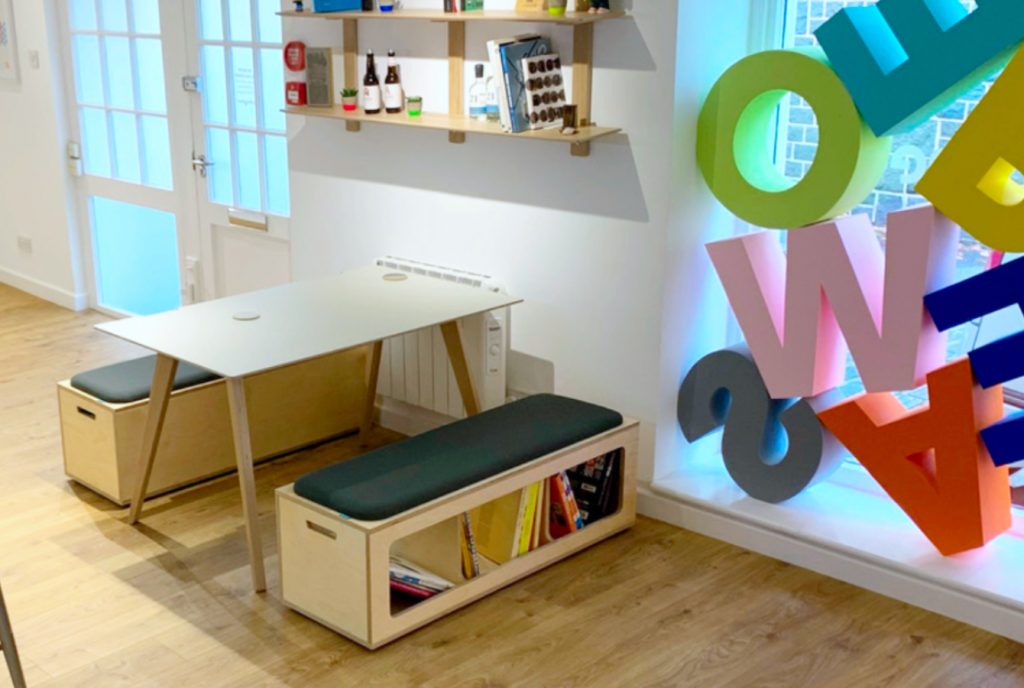Office reception breakout space, with wooden plywood storage benches, with upholstered seat pads in grey fabric